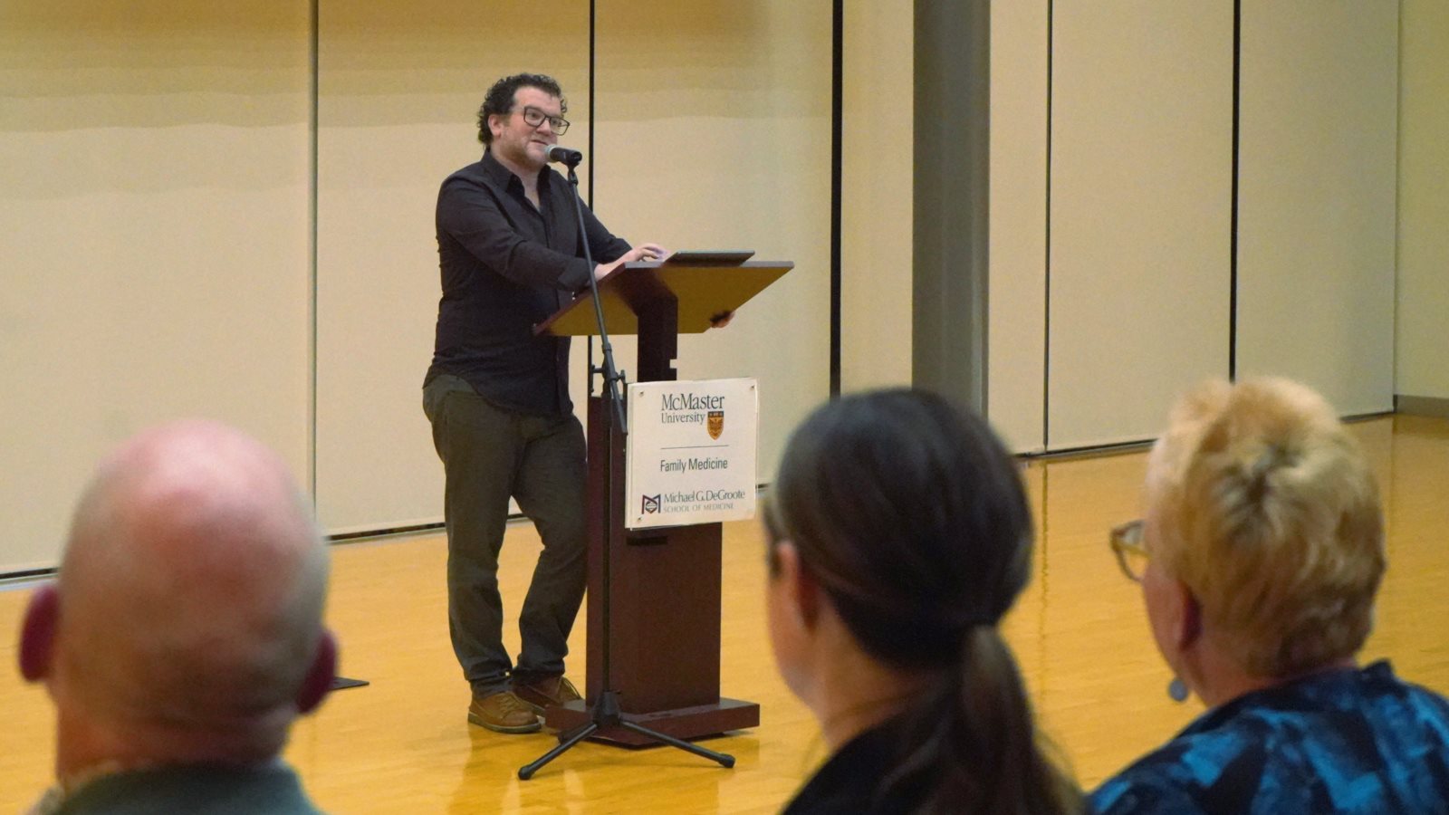 Pádraig Ó Tuama speaking at a podium. Three audience members are seen over their shoulders.